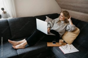 Smiling woman using laptop on sofa while freelancing at home